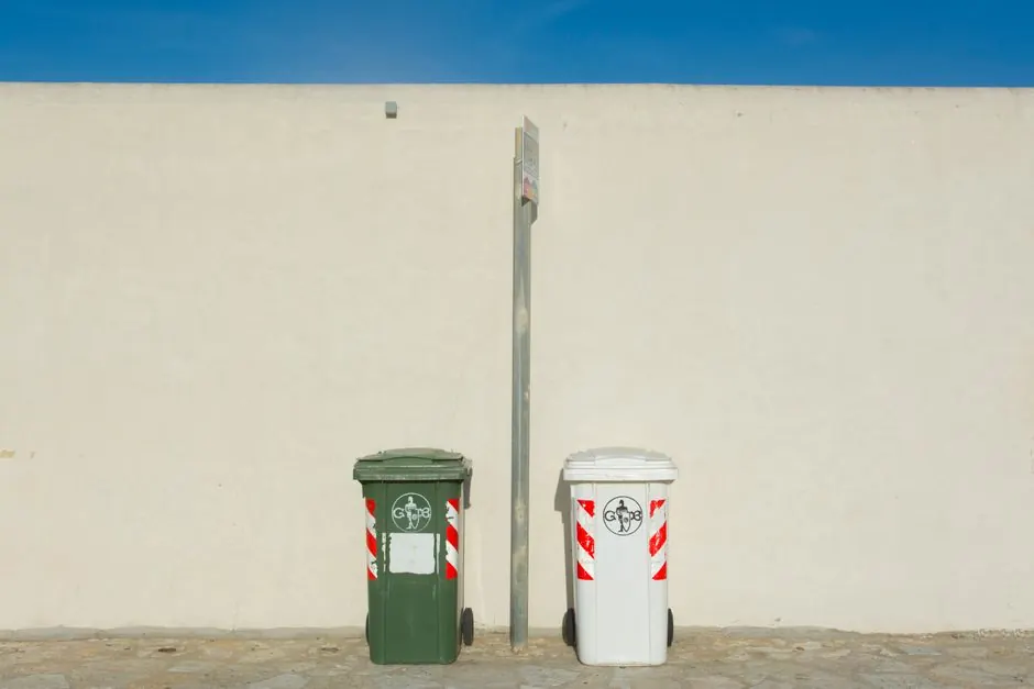 Two recycling bins next to a white wall under a clear blue sky, capturing urban simplicity.